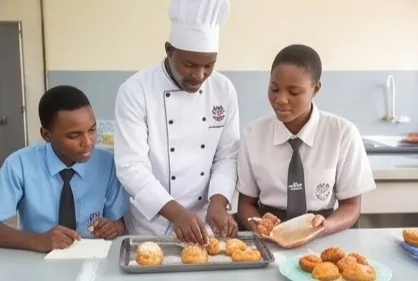 A chef guiding two students as they bake in a kitchen classroom