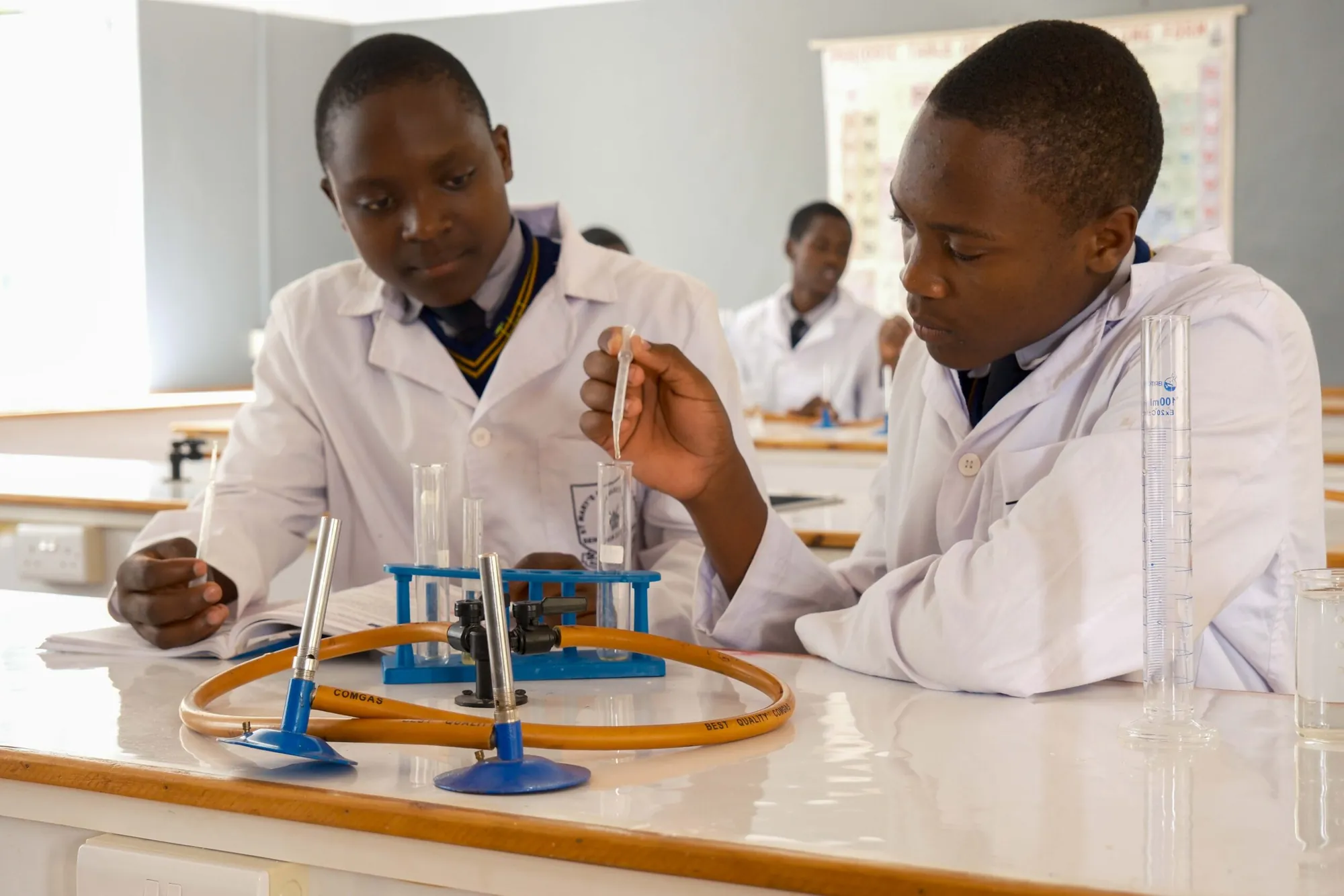 Two students in lab coats measuring liquids in test tubes