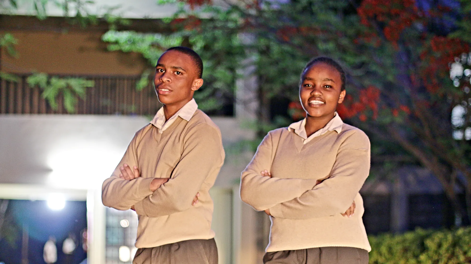 Two senior students in beige uniforms standing with folded arms